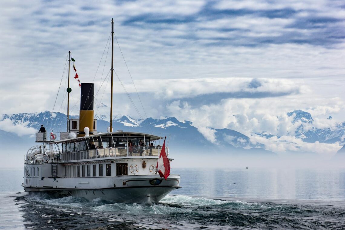 A luxury cruise ship sails on a misty lake with a snowy mountain backdrop.